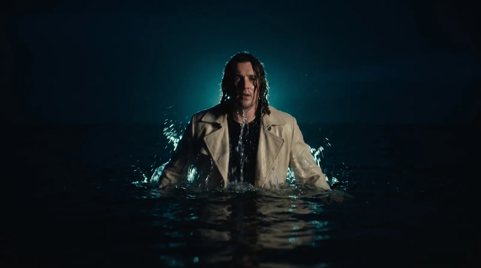 The man in the cream coat breaking the surface of a night sea, lit by a single teal rim light